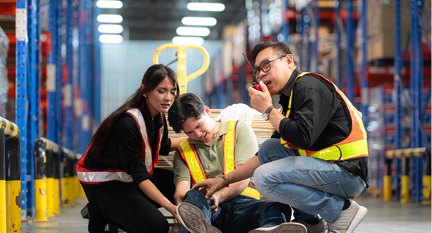 A man in a warehouse setting, injury, with co-workers assisting
